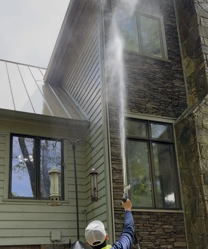 Junior soft washing the upper story of a stone and siding home